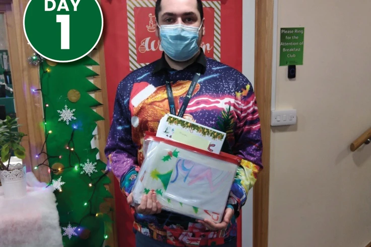 A man in a festive jumper holding pictures that will be donated to KMPT